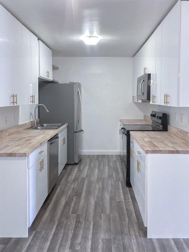 kitchen with dark wood-style floors, a sink, appliances with stainless steel finishes, wood counters, and white cabinetry