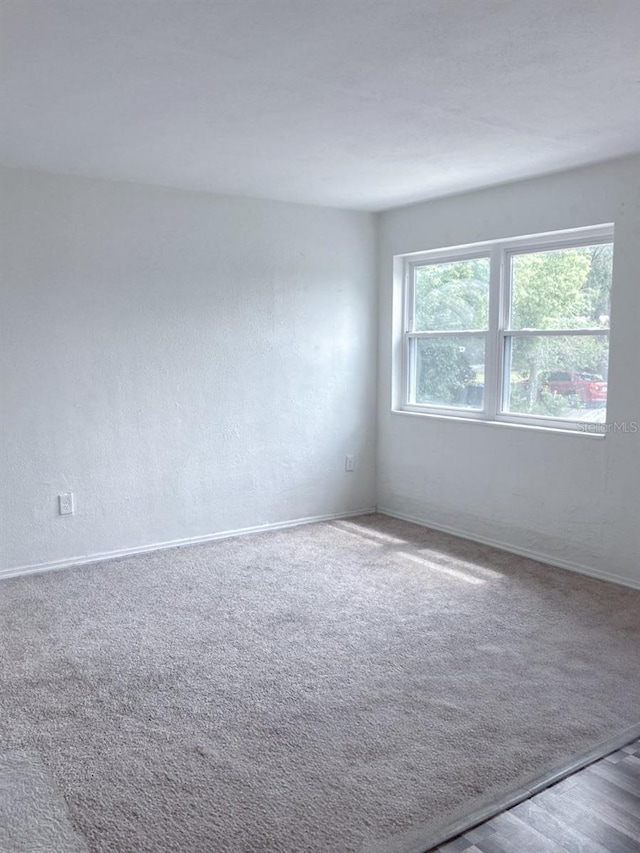 carpeted spare room featuring baseboards and a textured wall