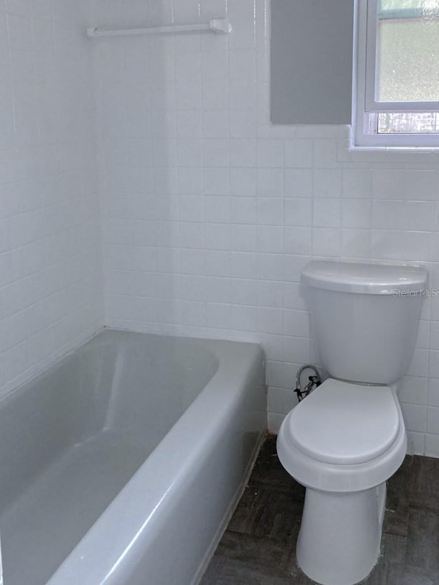 bathroom with a washtub, toilet, and tile walls