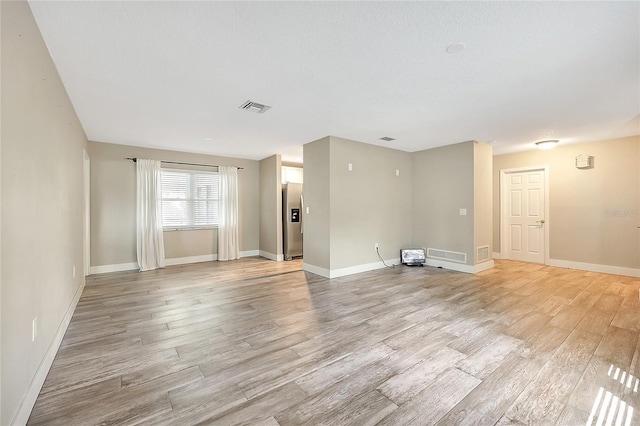 unfurnished living room featuring baseboards, visible vents, and light wood finished floors