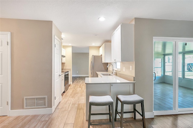 kitchen featuring visible vents, a breakfast bar, a sink, white cabinets, and appliances with stainless steel finishes