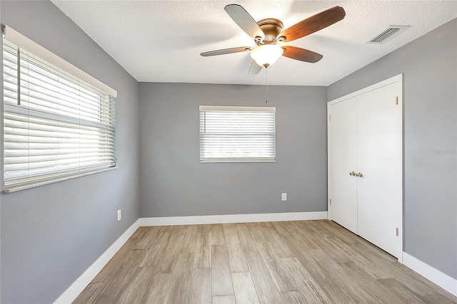 empty room featuring visible vents, a textured ceiling, a healthy amount of sunlight, and light wood finished floors