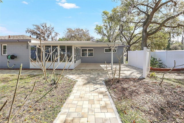 back of house with a sunroom, fence, a shingled roof, concrete block siding, and a patio area