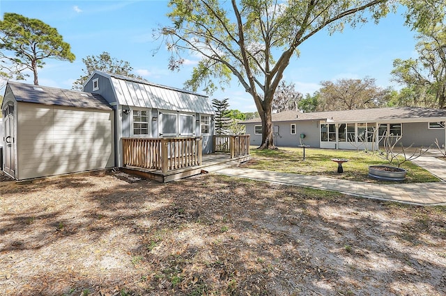 rear view of property with a gambrel roof, an outdoor fire pit, a yard, a sunroom, and a wooden deck