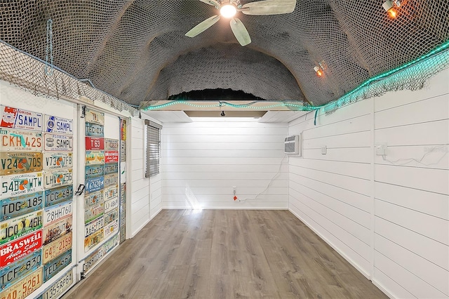 interior space with ceiling fan, wooden walls, wood finished floors, and a wall mounted AC