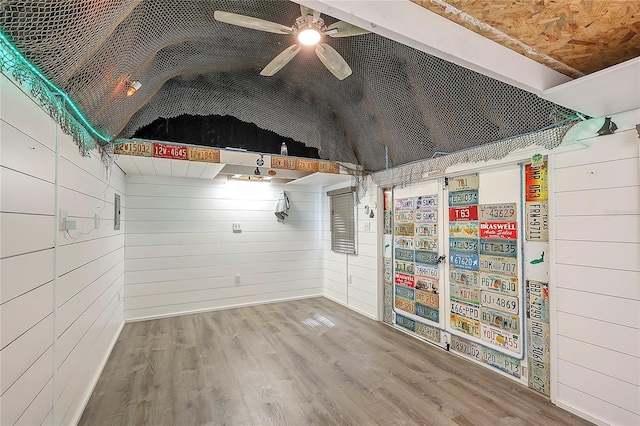 unfurnished room featuring a ceiling fan, lofted ceiling, wooden walls, and wood finished floors