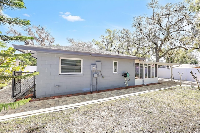 back of house featuring a patio area, a sunroom, concrete block siding, and fence