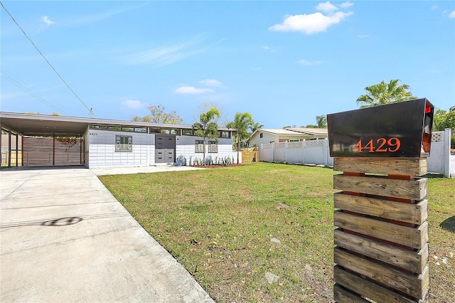 view of front of property featuring an attached carport, concrete driveway, a front lawn, and fence