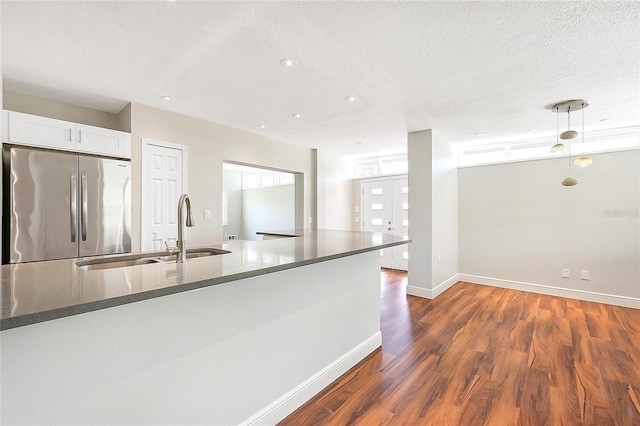 kitchen featuring baseboards, dark wood finished floors, a sink, stainless steel refrigerator, and white cabinetry