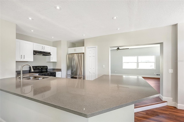 kitchen with black range with electric stovetop, under cabinet range hood, a sink, freestanding refrigerator, and dark stone counters