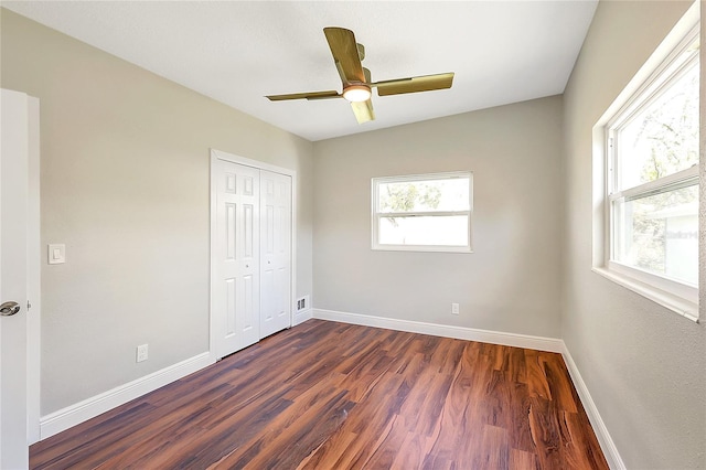 unfurnished bedroom featuring baseboards, multiple windows, and dark wood-style flooring