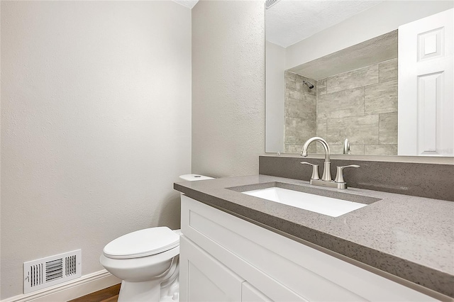 full bath with visible vents, toilet, a tile shower, a textured wall, and vanity