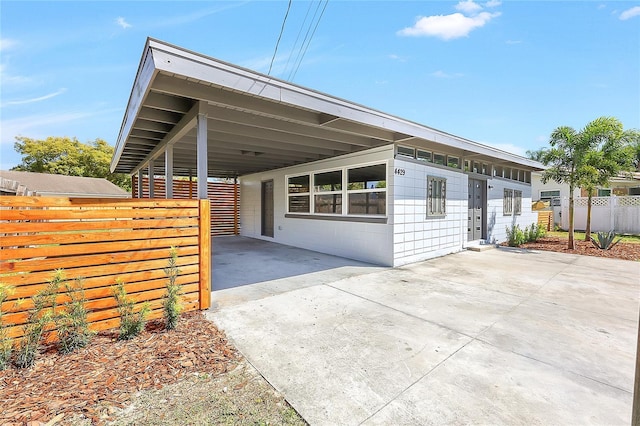 exterior space featuring an attached carport, driveway, concrete block siding, and fence