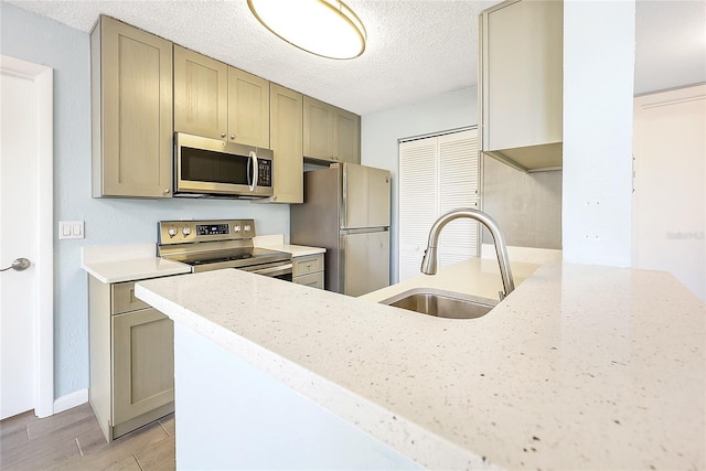 kitchen featuring light wood-style flooring, a sink, a textured ceiling, stainless steel appliances, and a peninsula