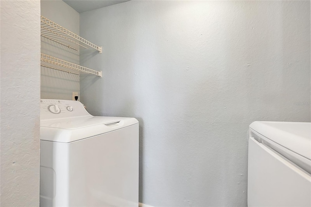 clothes washing area featuring a textured wall, laundry area, and washing machine and clothes dryer