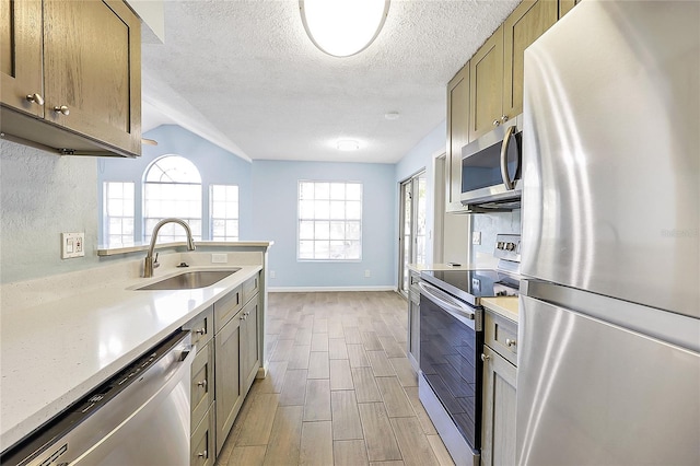 kitchen featuring wood finish floors, a sink, a textured ceiling, stainless steel appliances, and baseboards