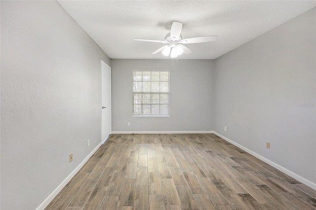 empty room with ceiling fan, wood finished floors, baseboards, and a textured ceiling