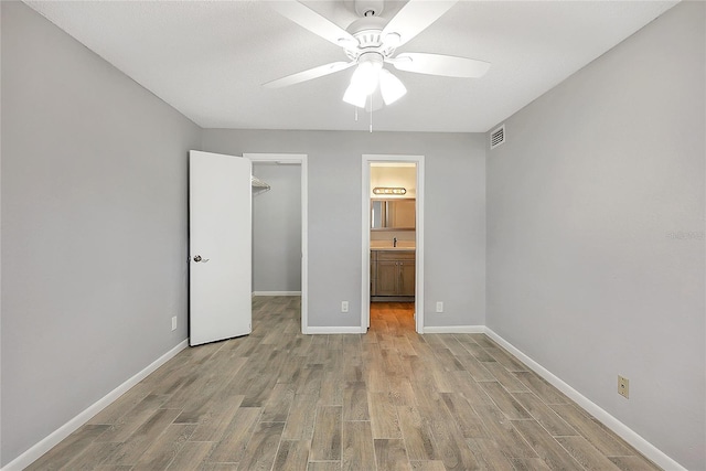 unfurnished bedroom featuring a closet, baseboards, a walk in closet, and light wood-style floors