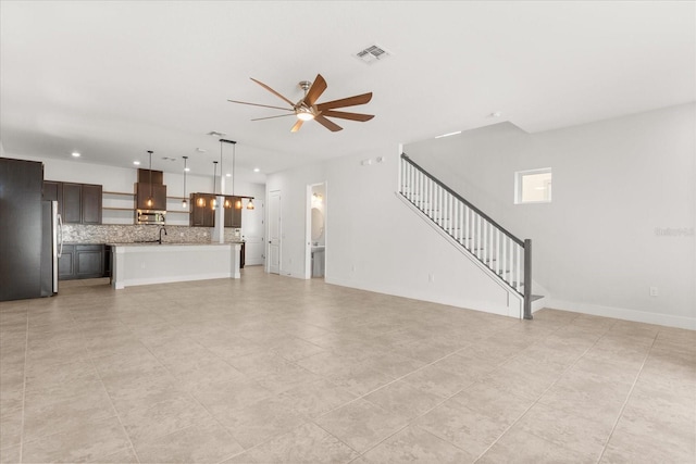 unfurnished living room with visible vents, baseboards, ceiling fan, stairs, and a sink