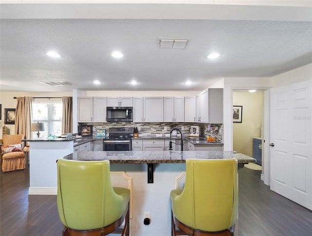 kitchen with tasteful backsplash, visible vents, appliances with stainless steel finishes, a peninsula, and dark wood-style flooring