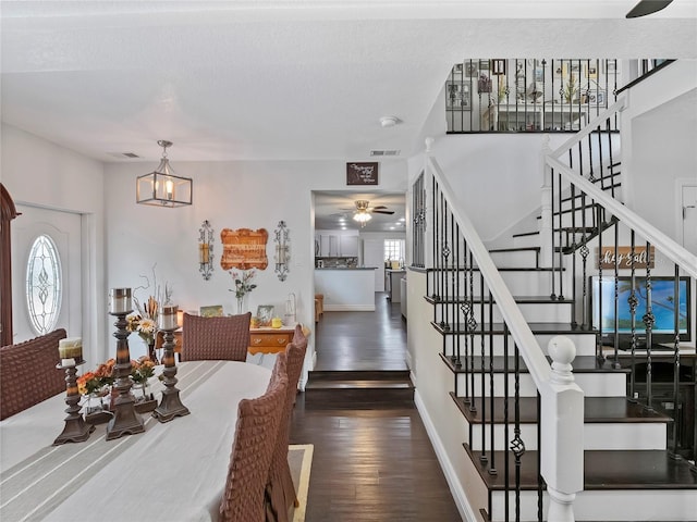 dining space with visible vents, baseboards, stairs, hardwood / wood-style floors, and ceiling fan with notable chandelier