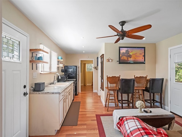 kitchen with baseboards, light countertops, light wood-style floors, a ceiling fan, and a sink