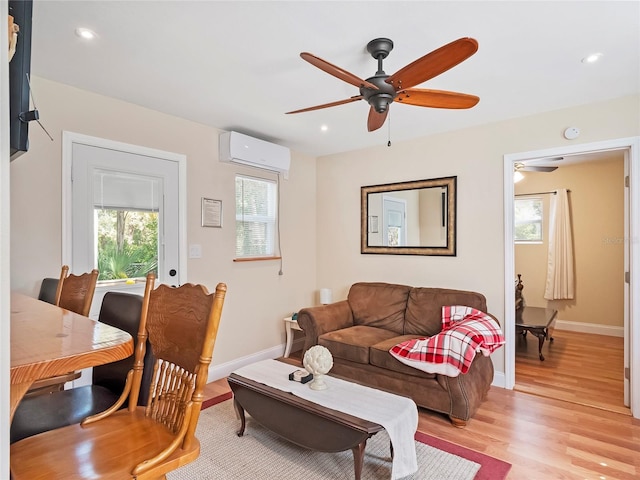 living room featuring a wall unit AC, baseboards, light wood-type flooring, and ceiling fan