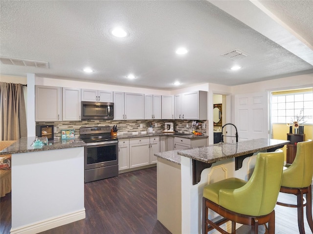 kitchen featuring dark wood-style flooring, a breakfast bar area, visible vents, and appliances with stainless steel finishes