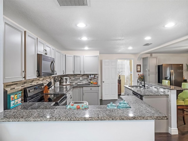 kitchen with visible vents, a kitchen island with sink, backsplash, stainless steel appliances, and a peninsula