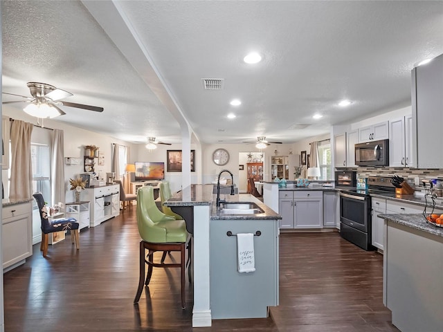 kitchen with visible vents, a kitchen bar, electric range, a ceiling fan, and a sink