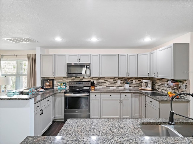 kitchen with visible vents, stone counters, a peninsula, stainless steel appliances, and a sink