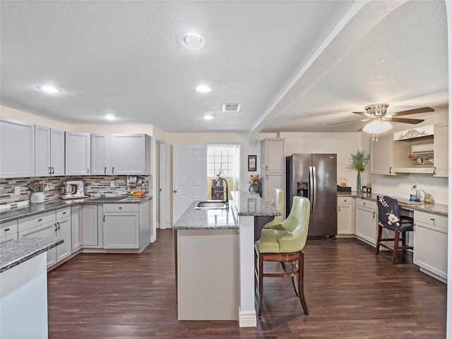 kitchen with a kitchen bar, stainless steel refrigerator with ice dispenser, dark wood-style flooring, and a sink