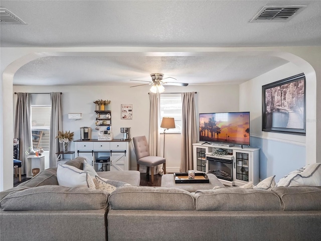 living room with arched walkways, visible vents, plenty of natural light, and a textured ceiling