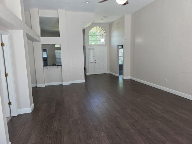 foyer entrance featuring dark wood finished floors, a ceiling fan, baseboards, and a towering ceiling