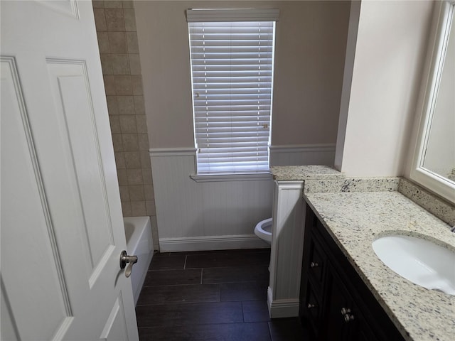 full bath with vanity, wood finished floors, a wainscoted wall, a bathing tub, and toilet