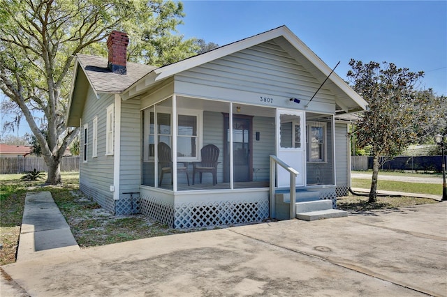 bungalow-style home with covered porch, a chimney, and fence