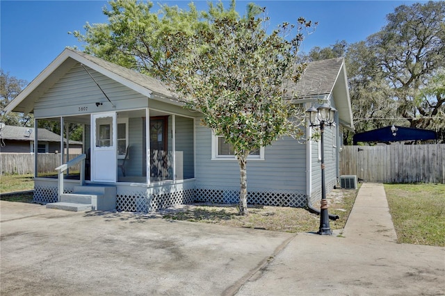 bungalow-style home with central air condition unit, covered porch, and fence