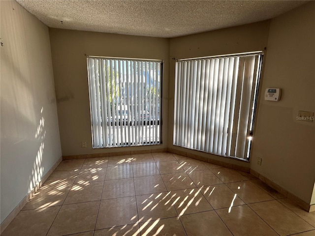 tiled spare room featuring a textured ceiling and baseboards