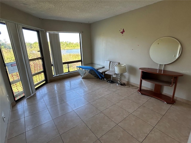 sitting room featuring tile patterned floors, baseboards, a water view, and a textured ceiling