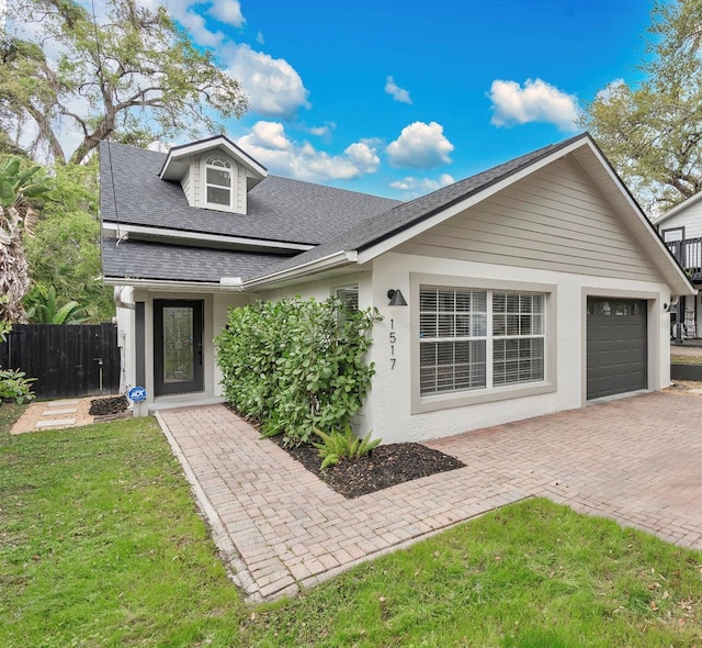 view of front facade featuring a front lawn, decorative driveway, fence, a shingled roof, and a garage