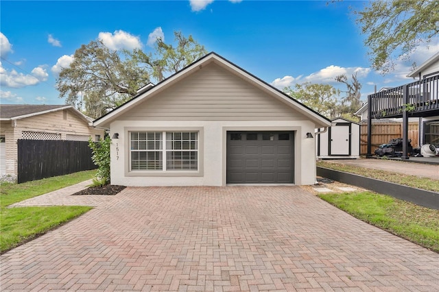 garage with decorative driveway, a storage shed, and fence