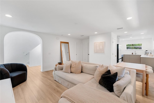 living area featuring recessed lighting, visible vents, arched walkways, and light wood-style floors