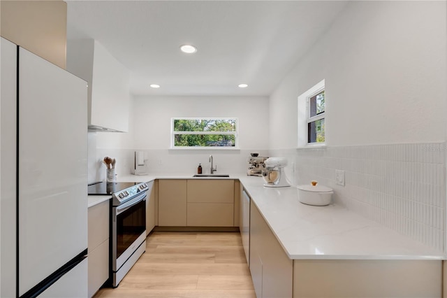 kitchen featuring light wood finished floors, stainless steel range with electric cooktop, freestanding refrigerator, modern cabinets, and a sink