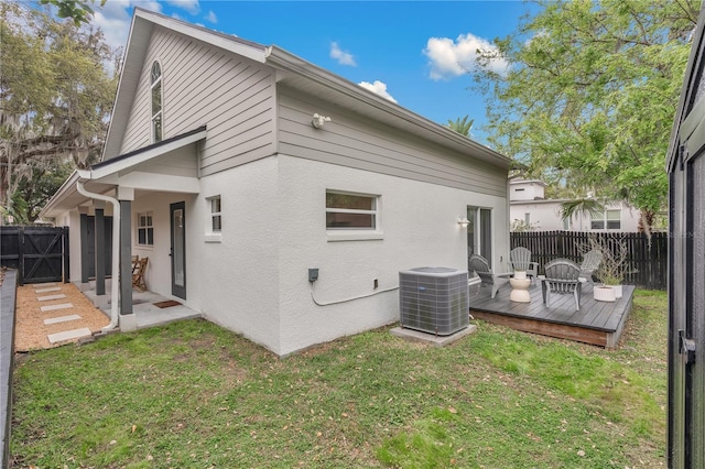 rear view of house with fence, a wooden deck, a yard, central AC, and stucco siding