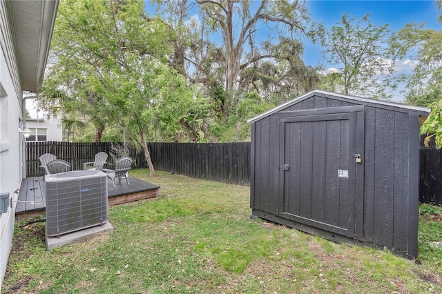 view of yard with an outbuilding, central AC unit, a wooden deck, a fenced backyard, and a storage shed