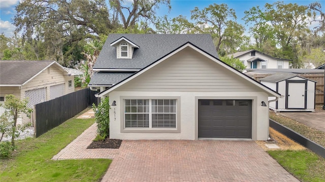 garage with decorative driveway, a storage shed, and fence