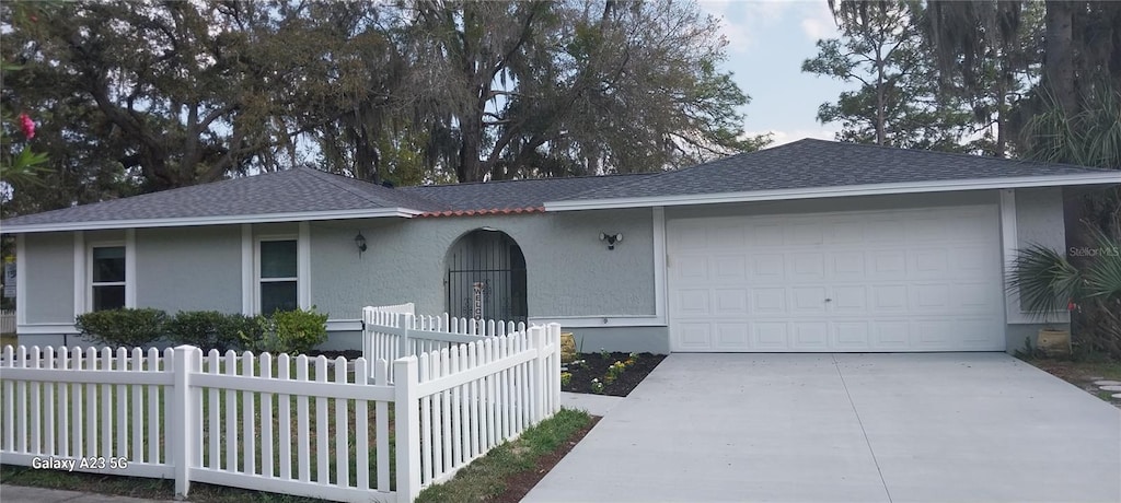 ranch-style house featuring concrete driveway, fence, a garage, and stucco siding