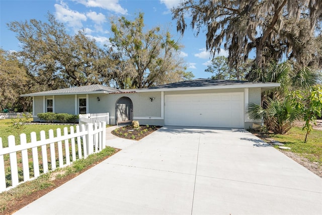 ranch-style home featuring a fenced front yard, driveway, an attached garage, and stucco siding