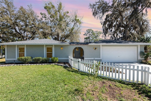 ranch-style home featuring a fenced front yard, concrete driveway, a front yard, stucco siding, and an attached garage