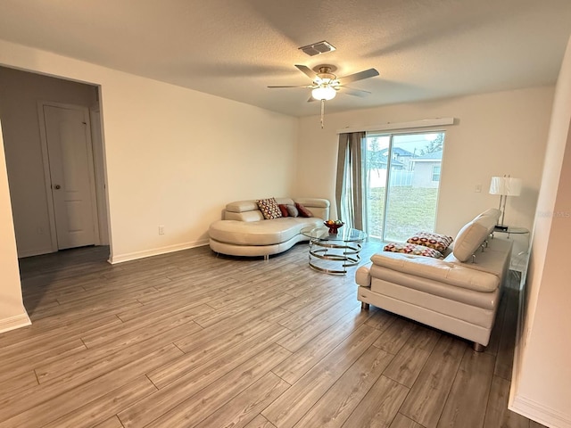 living room with light wood finished floors, visible vents, baseboards, ceiling fan, and a textured ceiling